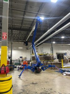 This image shows an atrium boom lift being used to reach over equipment in a warehouse.